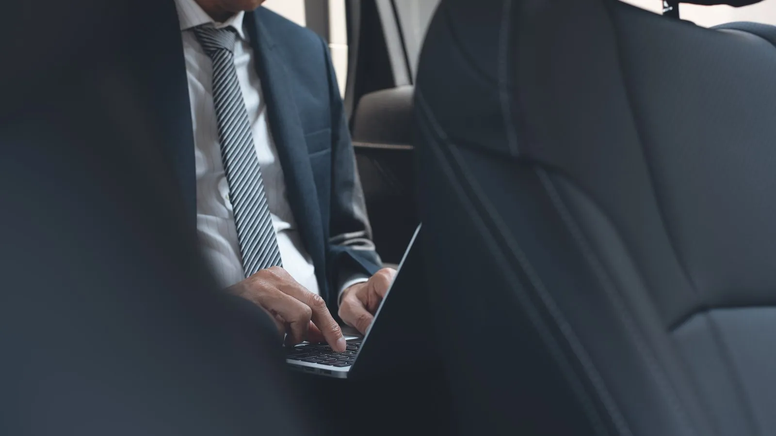 Business traveller working on a laptop in the back seat of a car